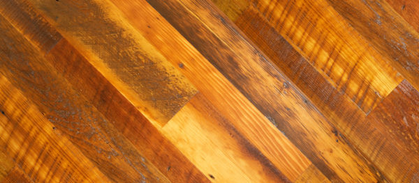 A close-up of a wooden surface, "Rocky Mountain Mosaic," shows diagonal planks in varying shades of brown. The texture highlights natural grain, knots, and weathering, creating a rustic and warm appearance reminiscent of a mountain landscape.