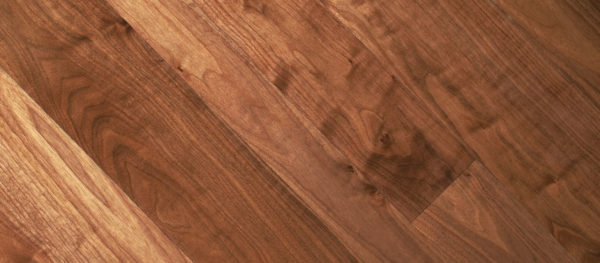 A close-up of Premium Walnut flooring reveals a rich, diagonal walnut color with visible grain patterns. The subtle texture and tone variations enhance its warm, rustic appeal.
