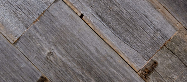 Close-up of Reclaimed Grey Barn Wood Siding arranged diagonally, highlighting rustic texture with visible grain patterns and knots. The aged wood displays gray tone variations and slightly rough surfaces.