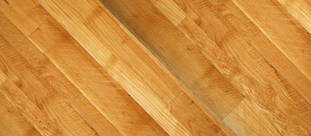 Close-up of Rustic White Oak flooring featuring light brown planks with visible gaps. The natural grain texture is prominent, and the boards are arranged diagonally.