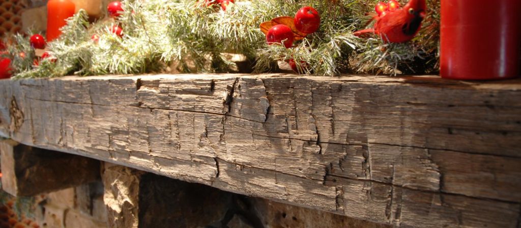 A decorative barn beam mantel adorned with pine branches, red berries, and red candles. The wood appears rustic and weathered, adding a cozy, festive ambiance to your home decor.