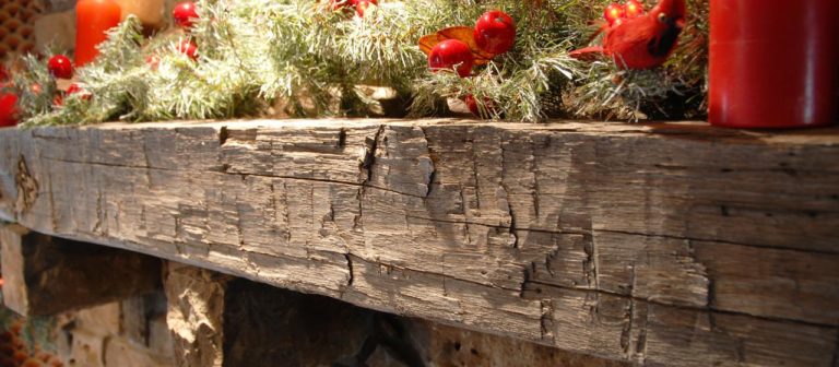 A decorative barn beam mantel adorned with pine branches, red berries, and red candles. The wood appears rustic and weathered, adding a cozy, festive ambiance to your home decor.