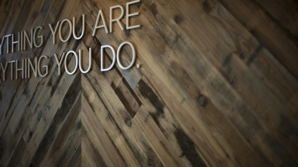 Close-up of a wooden wall in a modern work space design, featuring an incomplete motivational quote. The wall showcases mixed wood tones arranged in a diagonal pattern, adding a sleek and inspiring touch to the environment.