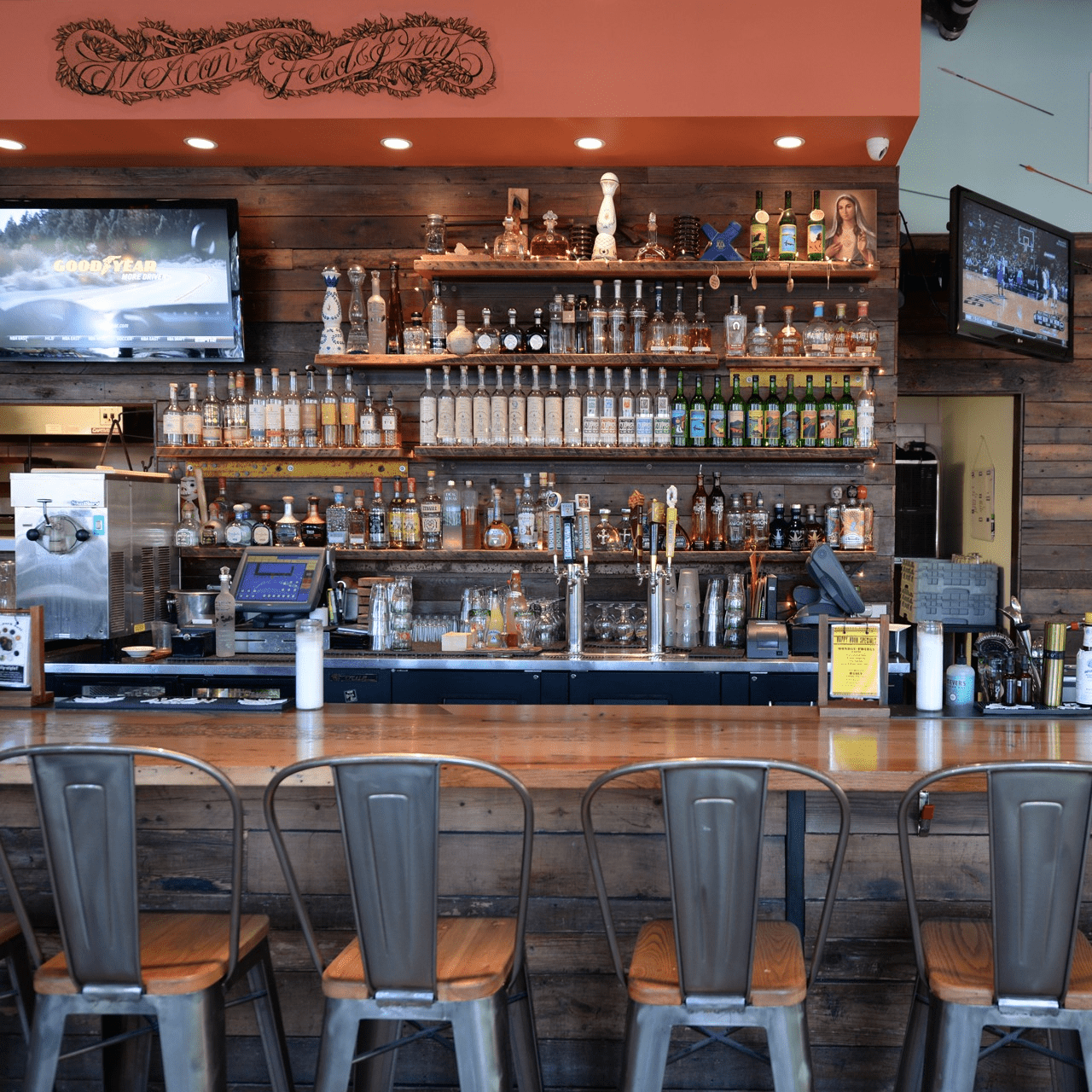 Liquor bottles on shelves behind a bar with a wood wall panel backsplash.