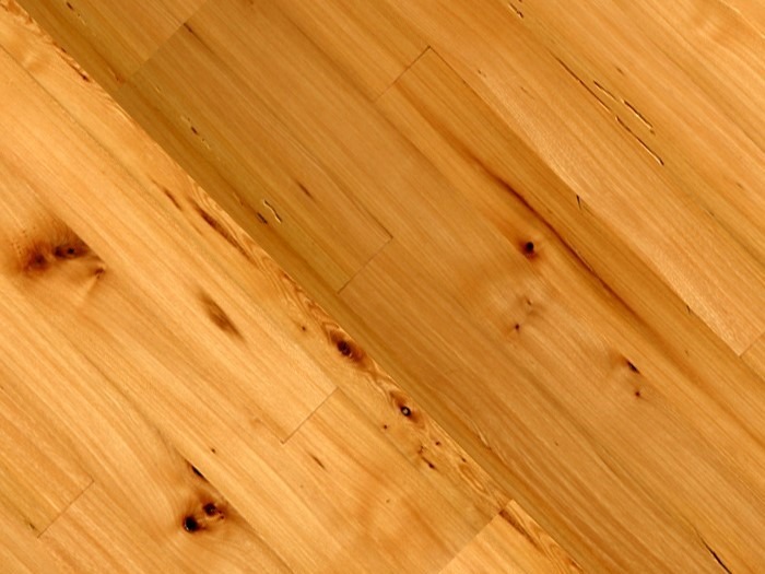 Close-up of a light wooden floor with a polished finish, showcasing natural grain patterns and small knots. The planks are arranged diagonally, emphasizing the texture and color variations in the wood—a true inventory special for those seeking elegance.