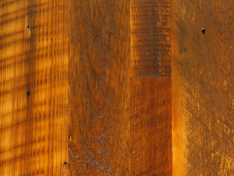 Close-up of a wooden surface with vertical planks showing varied textures and natural grain. Sunlight casts striped shadows across the wood, highlighting its warm, rich brown tones and rustic appearance—much like the unique finds in our inventory specials.