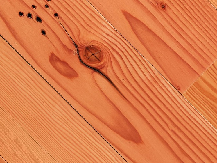 Close-up view of polished wooden floorboards featuring a prominent wood grain pattern. The surface has a warm, reddish-brown hue with visible knots and natural imperfections, enhancing the organic texture and appearance—perfect for adding character in inventory specials.
