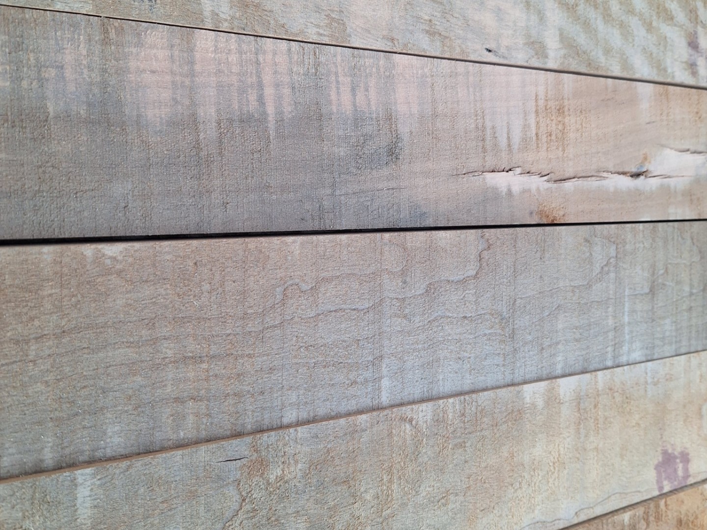 A close-up of a wooden surface with horizontal planks reveals natural grain patterns and subtle color variations, perfect for unique inventory specials. The wood's worn appearance, visible texture, and small cracks add character to any liquidation collection.