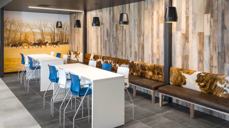 Modern cafeteria with long white tables, blue and white chairs, cowhide-patterned benches, wood-paneled walls, black pendant lights, and a large mural of running horses—a great best starting point for fresh design ideas.
