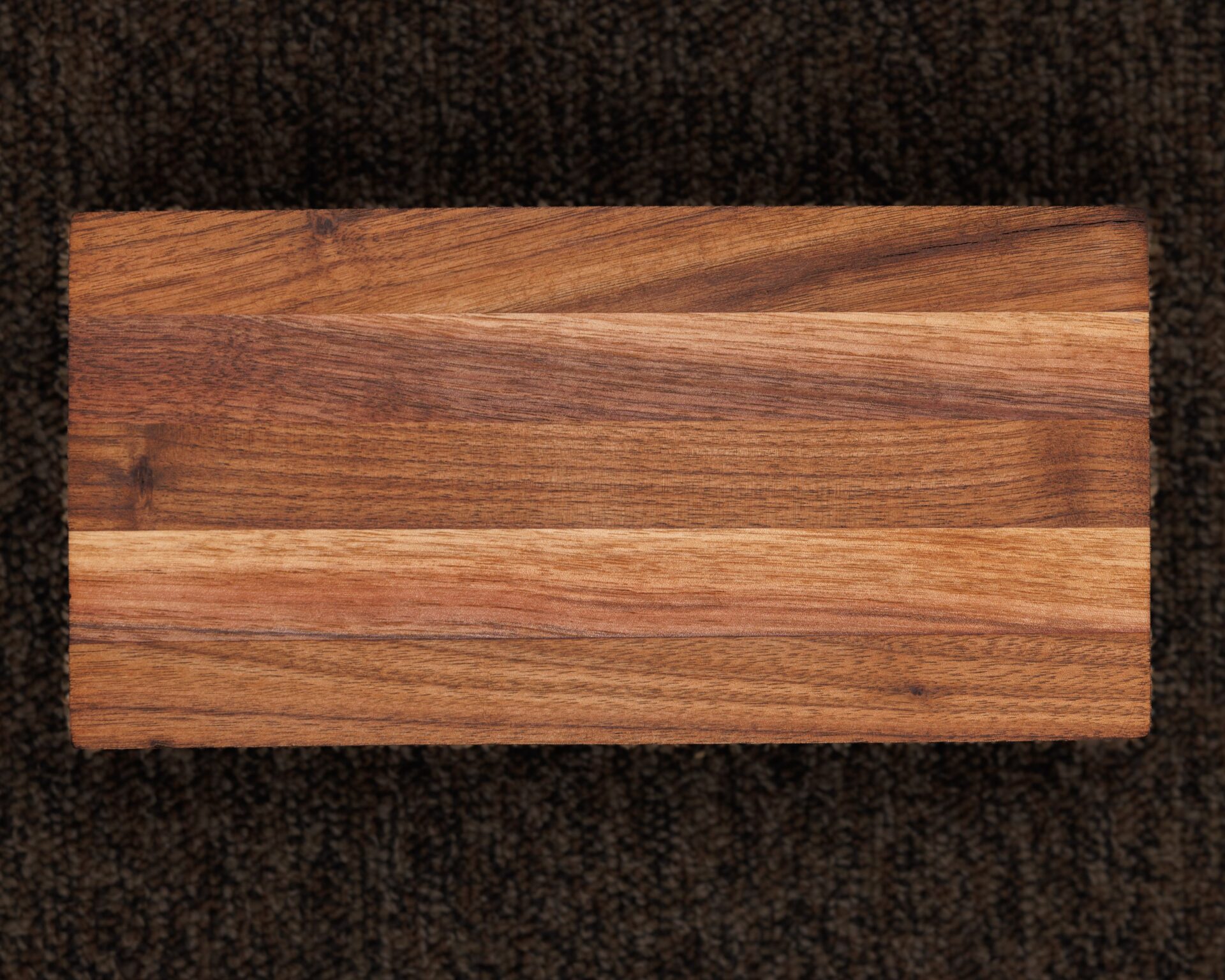 A 24 x 18 Custom Cutting Board with natural grain patterns rests on a dark, textured surface, shown in an overhead photo.