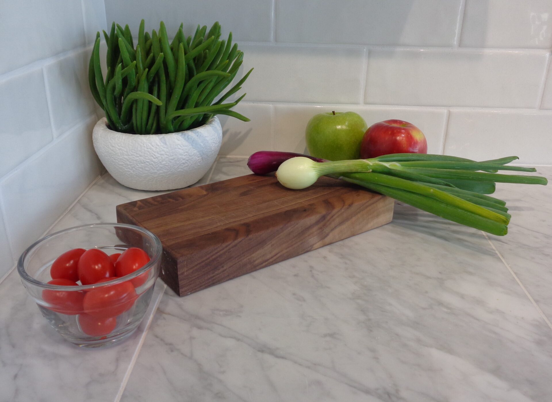 A 10 x 5 Custom Cutting Board with green onions, apple, onion, cherry tomatoes & a potted plant.