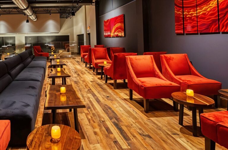 Modern lounge with orange chairs, wooden tables, and small glowing candles with Elmwood flooring.